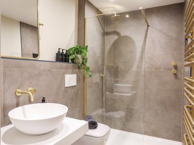 A bathroom with a white round sink a wall-mounted faucet a toilet with a folded towel a glass shower enclosure and a plant on a ledge at The Hayloft in Llanfechell