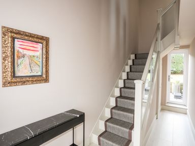 A hallway with stairs carpeted in grey with brown edges a black marble console table and framed artwork at The Hayloft in Llanfechell