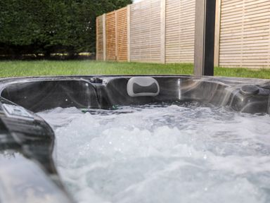 A bubbling outdoor hot tub with a headrest and wooden fencing in the background at The Hayloft in Llanfechell