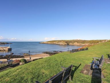 Benches on a grassy hill overlooking a bay with a beach and a stone pier at The Hayloft in Llanfechell