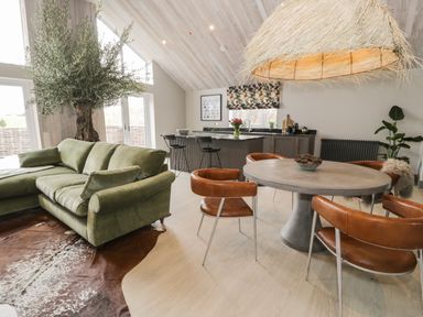 An open living space with a green sectional sofa brown leather chairs a round table and a kitchen island at Garden House in Llanfechell