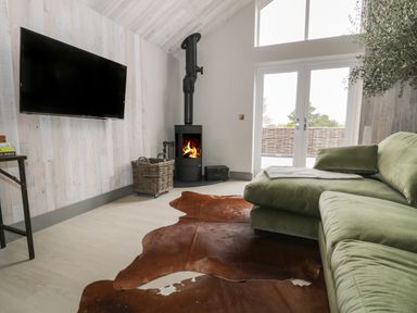 A living room with a green sectional sofa a wood stove a wall mounted tv and glass doors at Garden House in Llanfechell