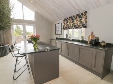 A kitchen with grey cabinets a black countertop a kitchen island with stools and flowers at Garden House in Llanfechell