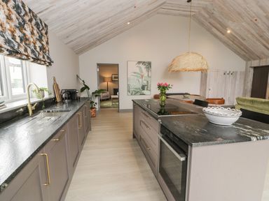 A kitchen with a black countertop island and cabinets with gold handles at Garden House in Llanfechell