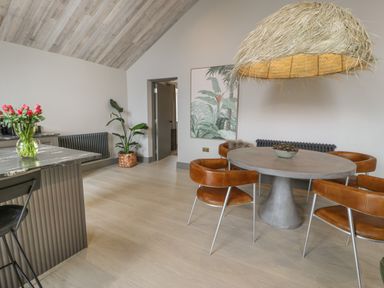A dining area with a round table and four brown chairs under a woven pendant light at Garden House in Llanfechell