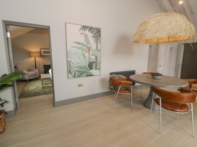 A dining room with a round table and four leather chairs next to a doorway leading to a sitting room at Garden House in Llanfechell