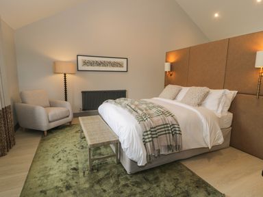 A bedroom with a bed a bench a beige armchair and lamps at Garden House in Llanfechell
