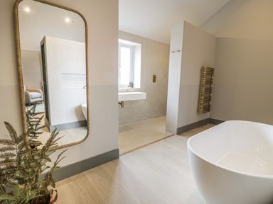 A bathroom with a freestanding bathtub a large mirror a plant and a window at Garden House in Llanfechell