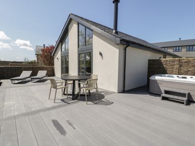 An outdoor patio area with a round table and four chairs two lounge chairs a hot tub and a building with large windows at Garden House in Llanfechell