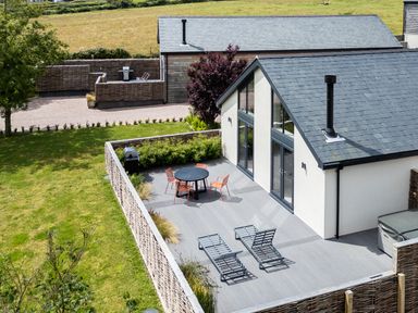 An outdoor patio with a round table with four chairs two sun loungers a barbecue grill and a small building in a grassy area at Garden House in Llanfechell