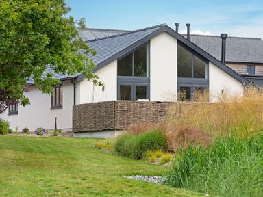 A house with large windows and a woven fence surrounded by grass and plants at Garden House in Llanfechell