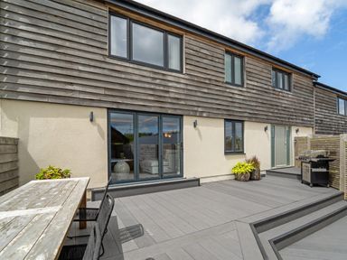 An outdoor patio area with a wooden table and chairs plants a barbecue and a building with multiple windows at The Farmhouse in Llanfechell