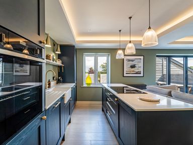 A kitchen with dark cabinets a white countertop pendant lights a window and a sofa at The Farmhouse in Llanfechell