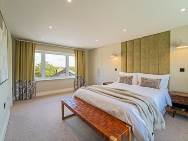 A bedroom with a large bed a bench at the foot of the bed bedside tables and windows with curtains at The Farmhouse in Llanfechell