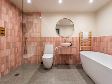 A bathroom with pink tiles a freestanding bathtub a toilet a round mirror and a shower at The Farmhouse in Llanfechell