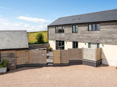 The exterior of a two-story building with wooden cladding and gravel ground at The Farmhouse in Llanfechell