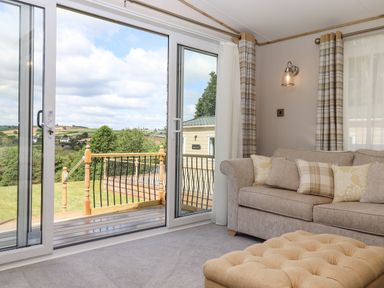 A living room with a sofa cushions ottoman and sliding glass door leading to a balcony at Ambleside in Cullompton