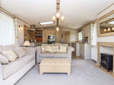 A living room with sofas cushions an ottoman and a fireplace connected to a kitchen with wooden cabinets at Ambleside in Cullompton