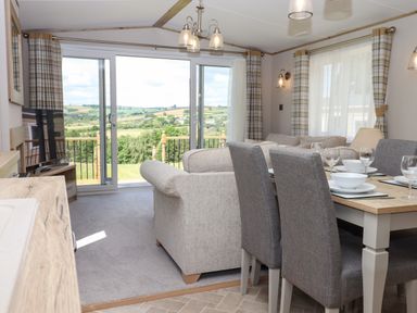 A living and dining area with sofas dining table set with plates and glasses and large sliding doors with a view at Ambleside in Cullompton
