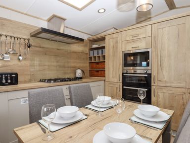 A kitchen with wooden cabinets a dining table set with white bowls plates and wine glasses and a stove with a range hood at Ambleside in Cullompton