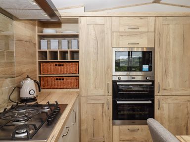 A kitchen with a gas stove kettle microwave oven and wooden cabinets at Ambleside Cullompton