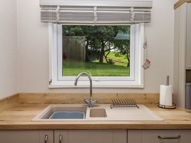 A kitchen sink under a window with a dish rack and paper towel holder on the countertop at Ambleside in Cullompton