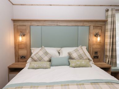 A bedroom with a double bed featuring a wooden headboard with teal upholstery and plaid pillows at Ambleside in Cullompton