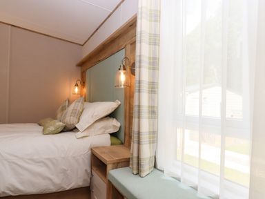 A bedroom with a bed next to a window with curtains and a small bedside table at Ambleside in Cullompton