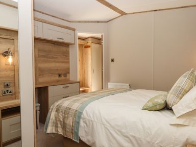 A bedroom with a bed with pillows and blanket a wooden dresser and a door leading to a closet at Ambleside in Cullompton
