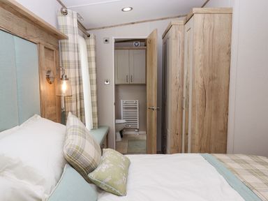A bedroom with a bed pillows headboard window curtains and a door opening to a bathroom at Ambleside in Cullompton