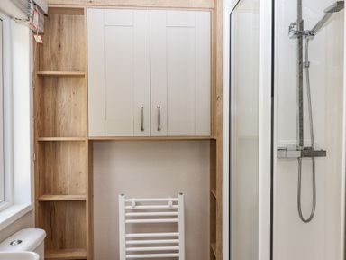 A bathroom with a shower enclosure a white towel radiator wooden shelves and a cabinet above the radiator at Ambleside in Cullompton