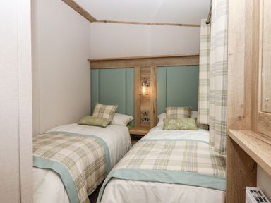 A bedroom with two single beds with plaid bed runners and pillows and a wooden headboard at Ambleside in Cullompton
