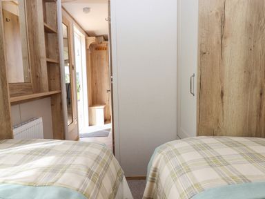 A bedroom with two single beds covered with plaid blankets a wooden wardrobe and a hallway with wooden hooks and a bench at Ambleside in Cullompton