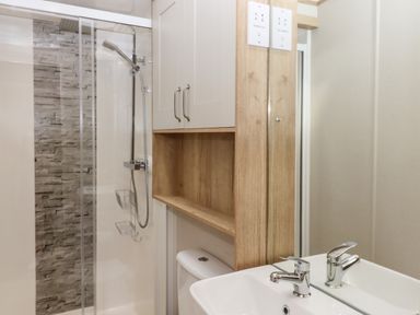 A bathroom with a shower area with stone wall tiles a sink a mirror and a wooden cabinet at Ambleside in Cullompton