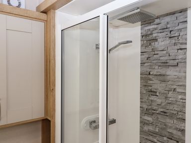A shower area with glass doors stone tile wall and wooden cabinet at Ambleside in Cullompton