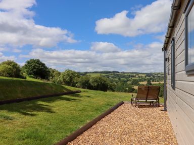 A patio chair outside a building with a grassy lawn and trees under a blue sky at Ambleside in Cullompton