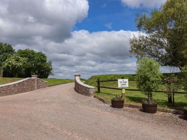 A gravel path with stone walls on the sides and a sign reading to the lake with wooden fence and trees in the background at Ambleside in Cullompton