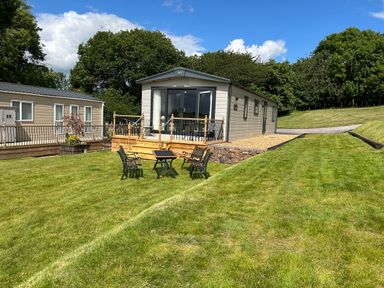 A garden with chairs and a table in front of two mobile homes surrounded by trees at Ambleside in Cullompton