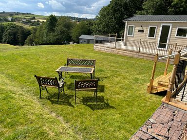 A grassy garden area with outdoor table and chairs near a raised deck and building at Ambleside in Cullompton