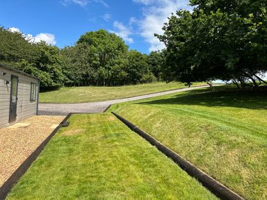 A lawn with a gravel pathway and trees next to a small building at Ambleside in Cullompton