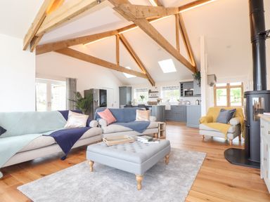An open living room and kitchen with exposed wooden beams sofas and a wood stove at Trevilges Cottage Trewennack near Helston