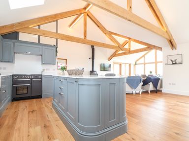 A kitchen with blue cabinets and wooden beams overlooking a living area at Trevilges Cottage in Trewennack near Helston