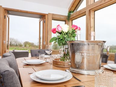 A dining table with plates glasses a champagne bucket and flowers in a room with wooden framed windows at Trevilges Cottage Trewennack near Helston