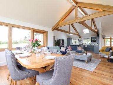 An open-plan dining and living area with gray chairs around a wooden table and sofas near the kitchen at Trevilges Cottage in Trewennack near Helston