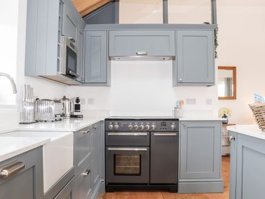 A kitchen with blue cabinets a black oven a silver microwave toaster kettle and coffee machine at Trevilges Cottage Trewennack near Helston