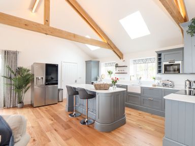 A kitchen with grey cabinets wooden beams and two bar stools at Trevilges Cottage Trewennack near Helston