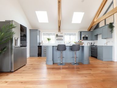 A kitchen with blue cabinetry wooden beams and two stools at the island at Trevilges Cottage Trewennack near Helston