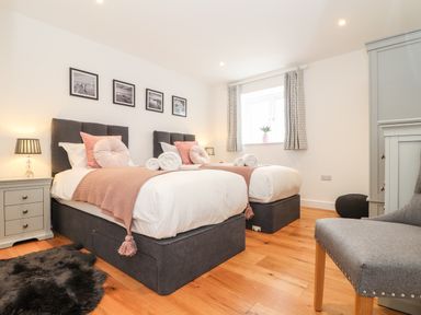 A bedroom with two single beds bedside tables lamps chair and wooden floor at Trevilges Cottage Trewennack near Helston