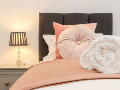 A bed with pillows and a blanket with a rolled towel on top next to a nightstand with a lamp at Trevilges Cottage in Trewennack near Helston
