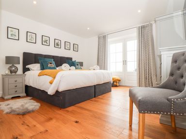 A bedroom with a double bed nightstands lamps and a gray upholstered chair at Trevilges Cottage Trewennack near Helston